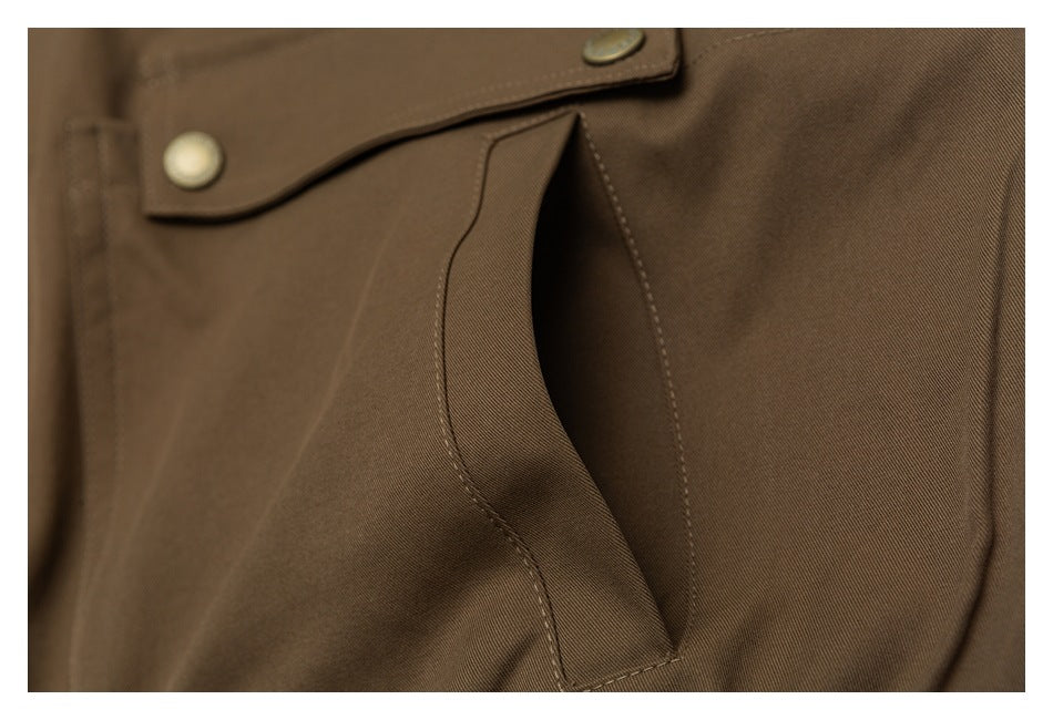 Close-up of a curved opening pocket on brown trousers, with a buttoned flap above it.
