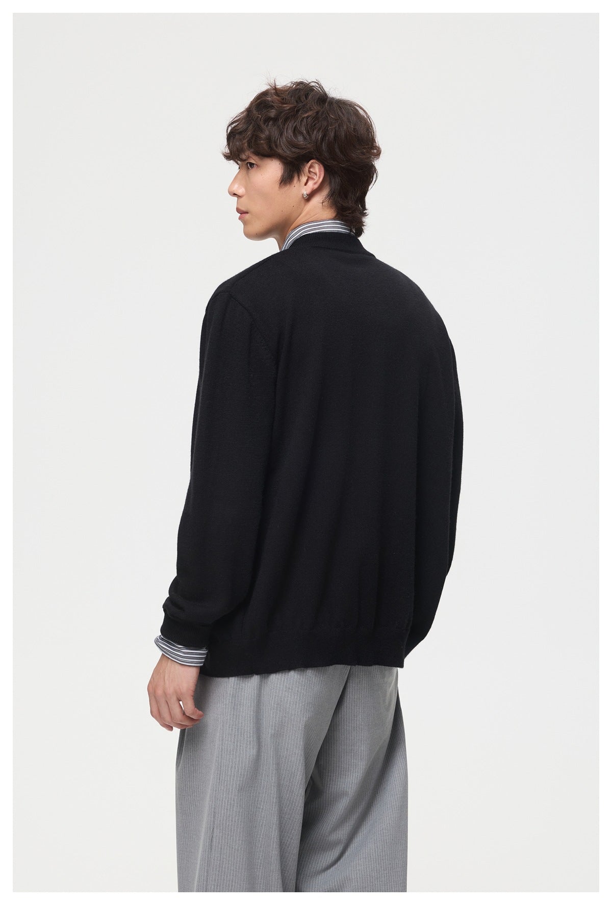 Model wearing a black cardigan, shown from the back with striped shirt cuffs and collar visible.