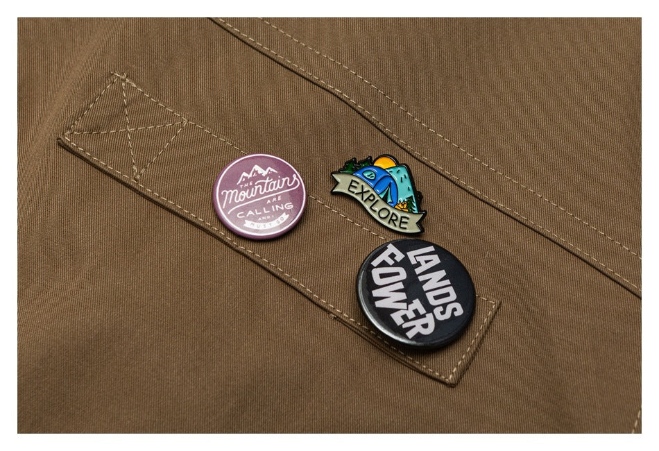 Close-up of three colorful English-text pins attached to a stitched panel on a brown garment.