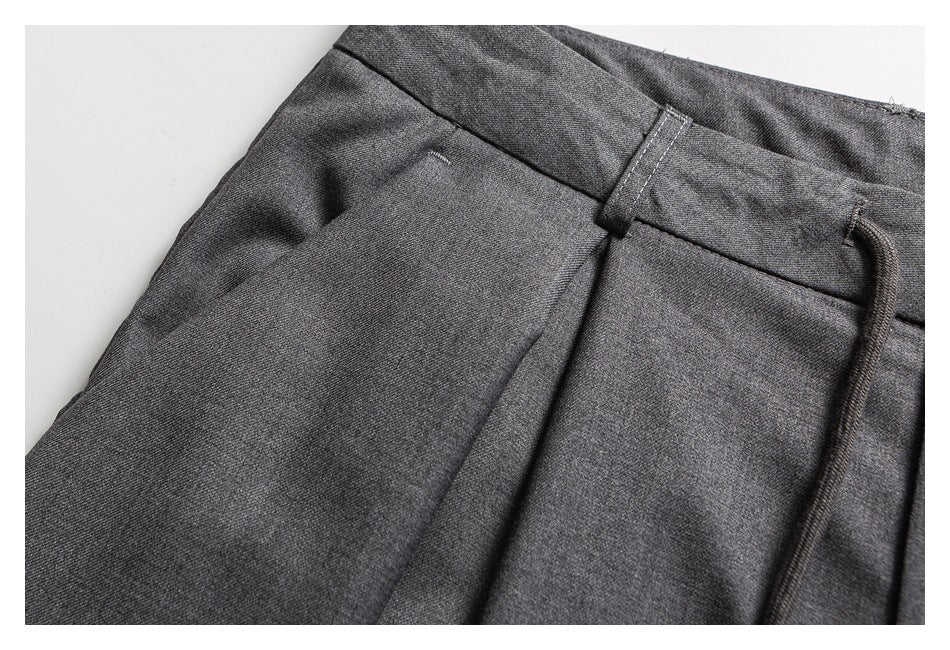 Close-up of charcoal gray trousers showing a belt loop, waistband seam, pleat, and drawstring.