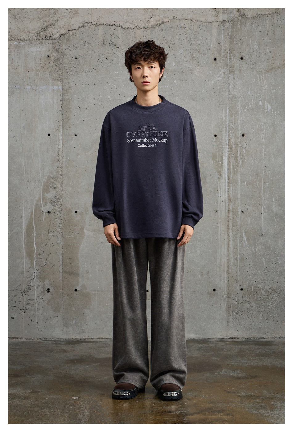 Model wearing a navy oversized crewneck sweatshirt with white chest text and loose gray trousers, shown full length.
