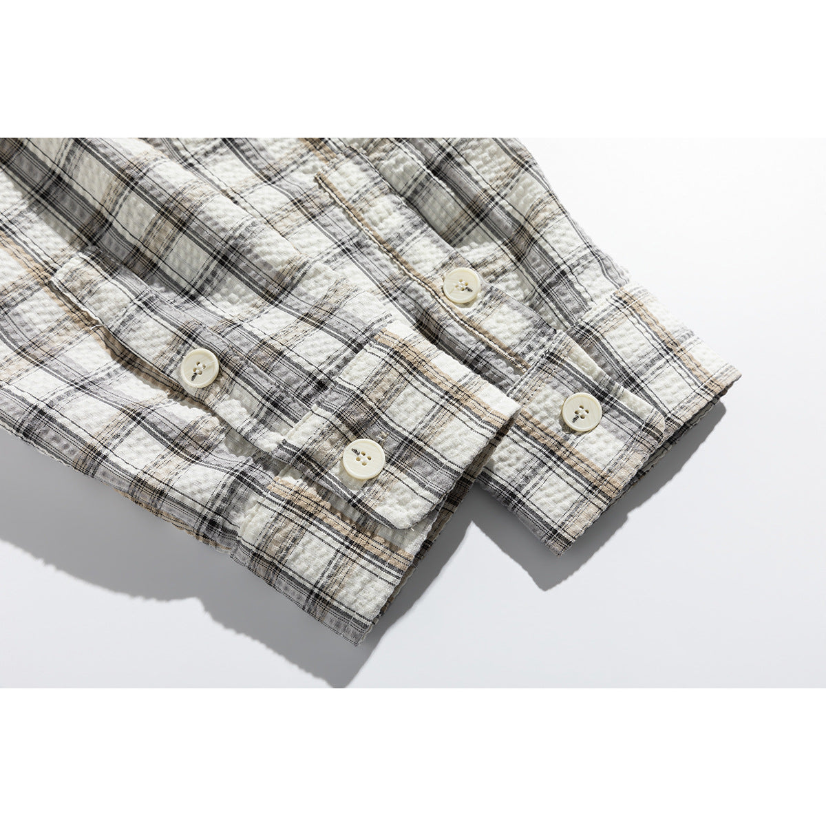 Close-up of the cream plaid shirt's buttoned cuffs and textured fabric.