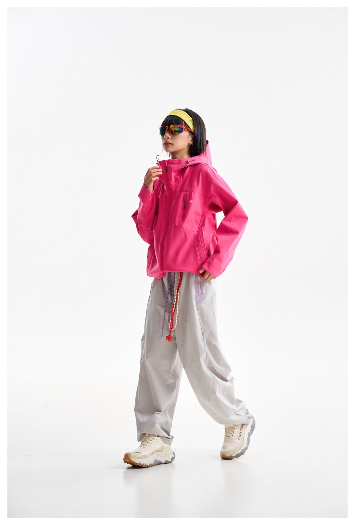Side view of a model wearing a bright pink hooded jacket and loose light gray trousers.