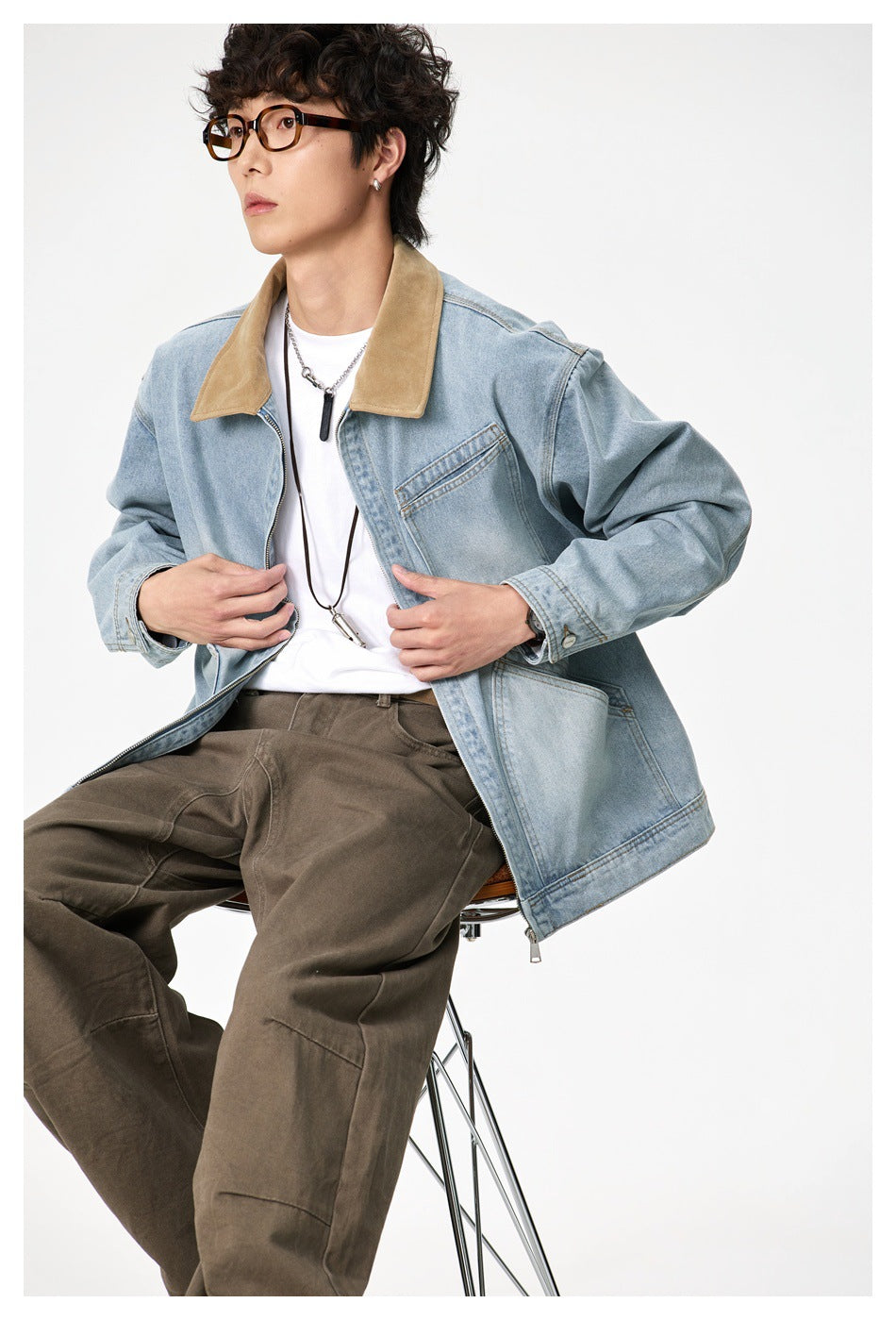 Seated model wearing an open light-wash denim jacket with a tan collar and chest and hip pockets.