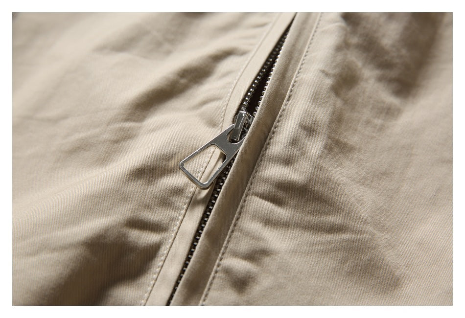 Close-up of a metal zipper and pull on beige jacket fabric.