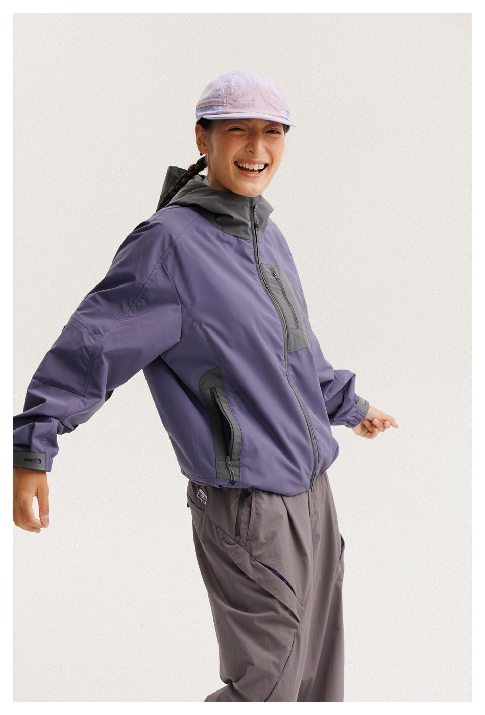 Closer view of a model wearing a purple hooded jacket with charcoal zip pockets and panels, paired with gray pants.
