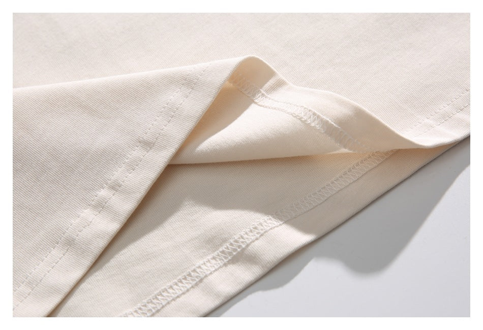 Close-up of the cream T-shirt’s folded bottom hem and visible overlock stitching.