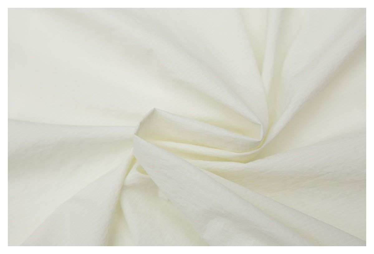 Close-up of softly draped ivory fabric showing its fine subtle texture.