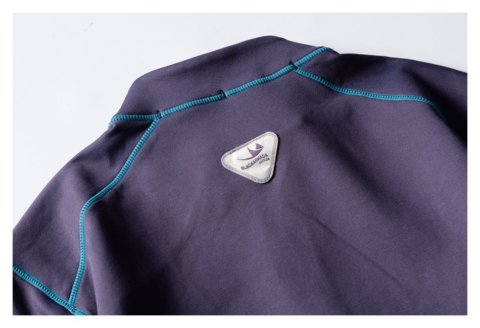 Close-up of the back of a dark purple garment with teal seam details and a small sewn patch.