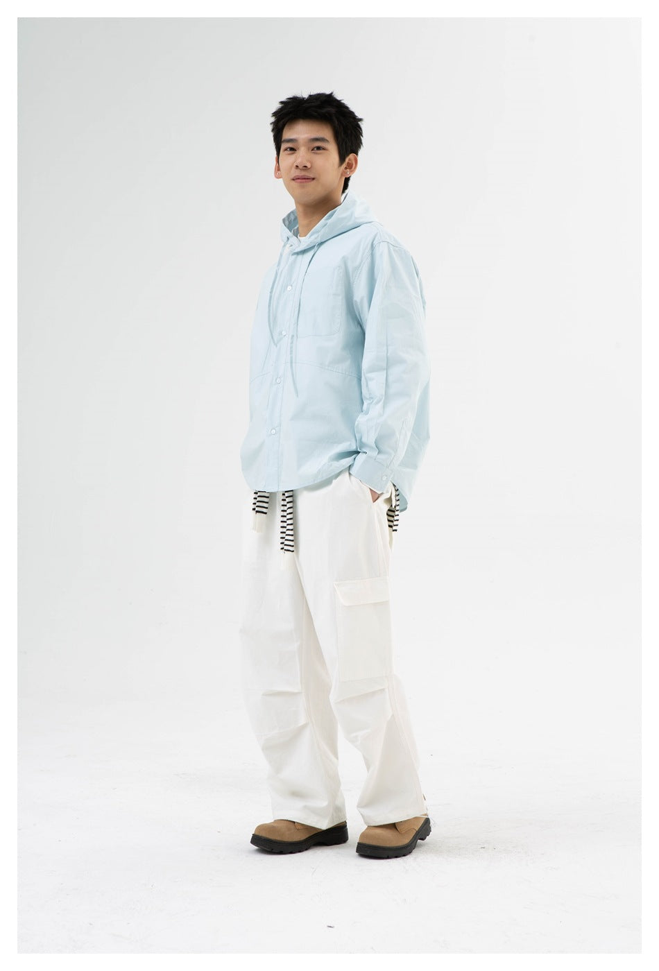 Model wearing light blue hooded button-front shirt with white cargo pants, front three-quarter view