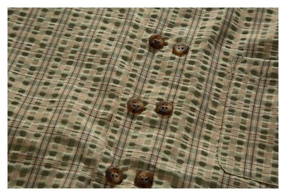 Close-up of the shirt front showing brown buttons, a patch pocket, and an olive and tan plaid pattern.