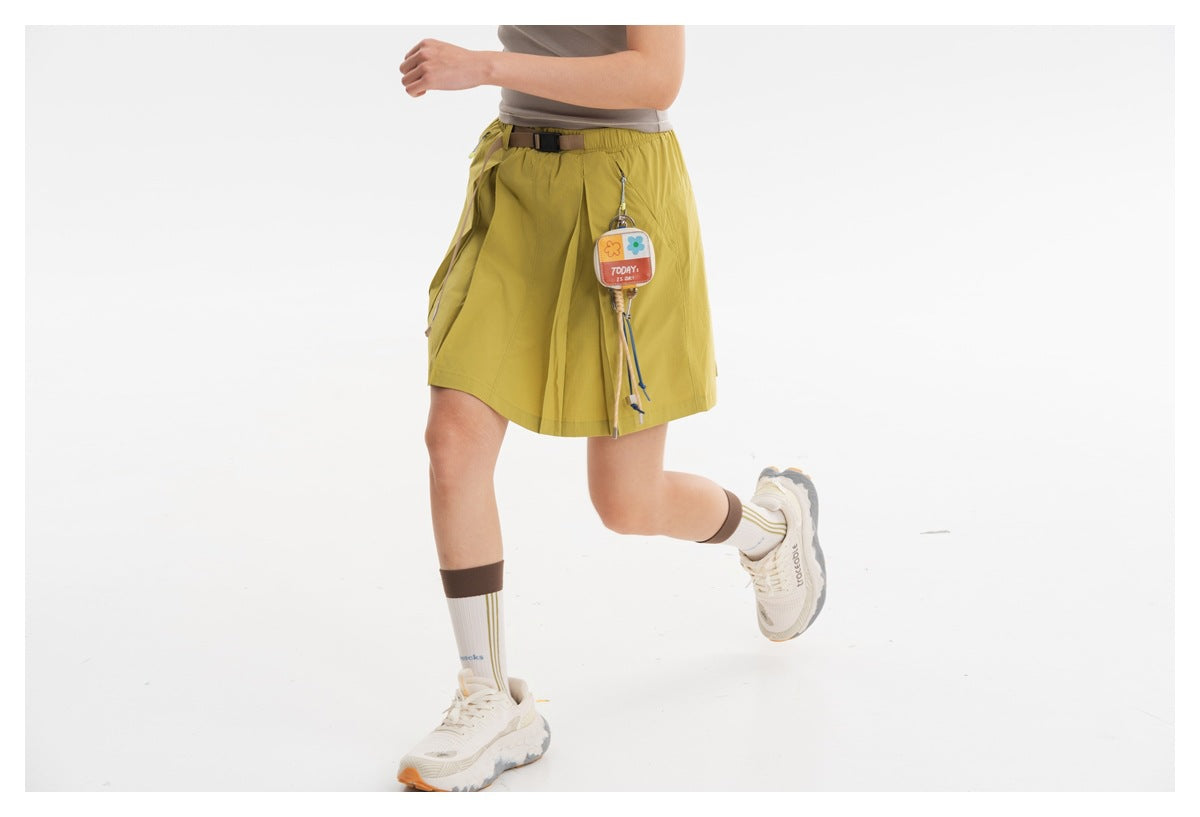 Model in a chartreuse pleated skort, shown from the back with an elastic waist, belt and dangling charm.