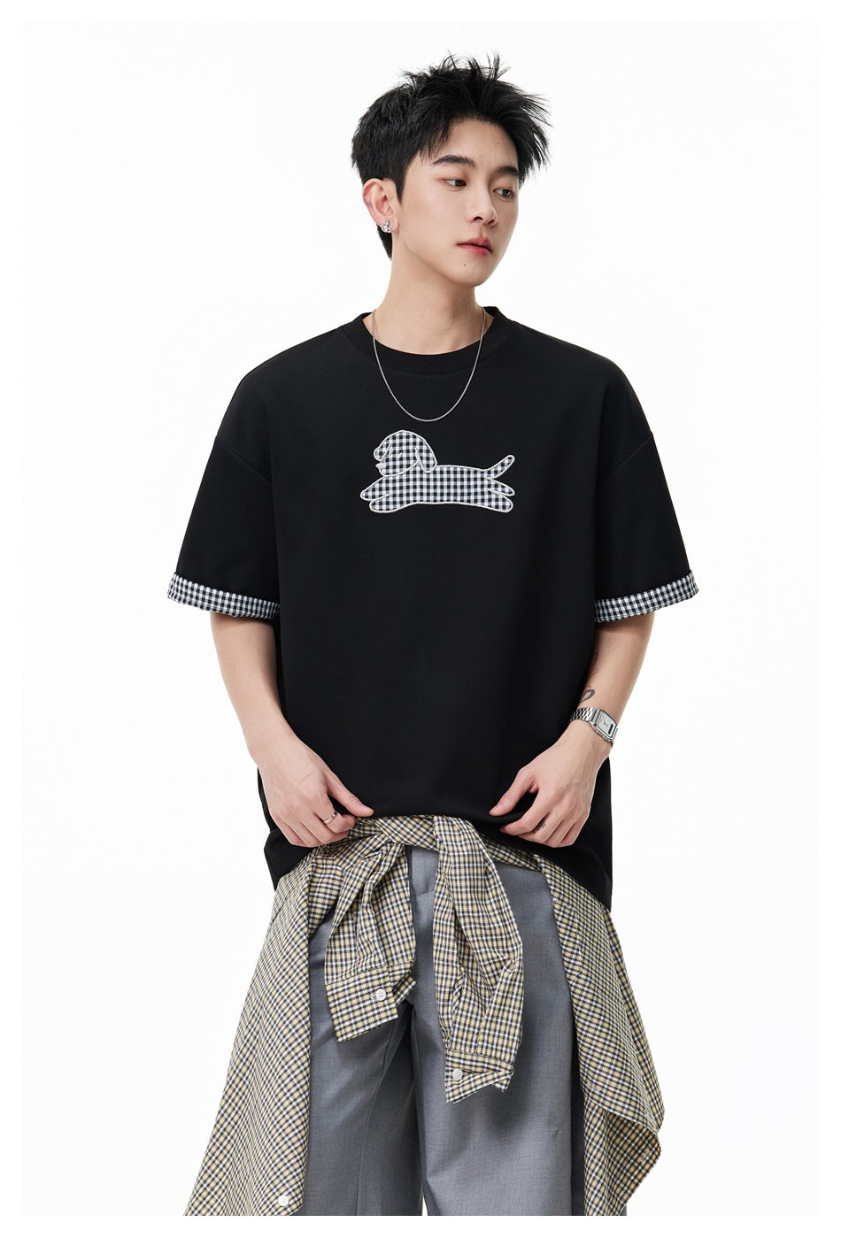 Man wearing a black T-shirt with a gingham dog graphic and checked sleeve cuffs, shown from the front.