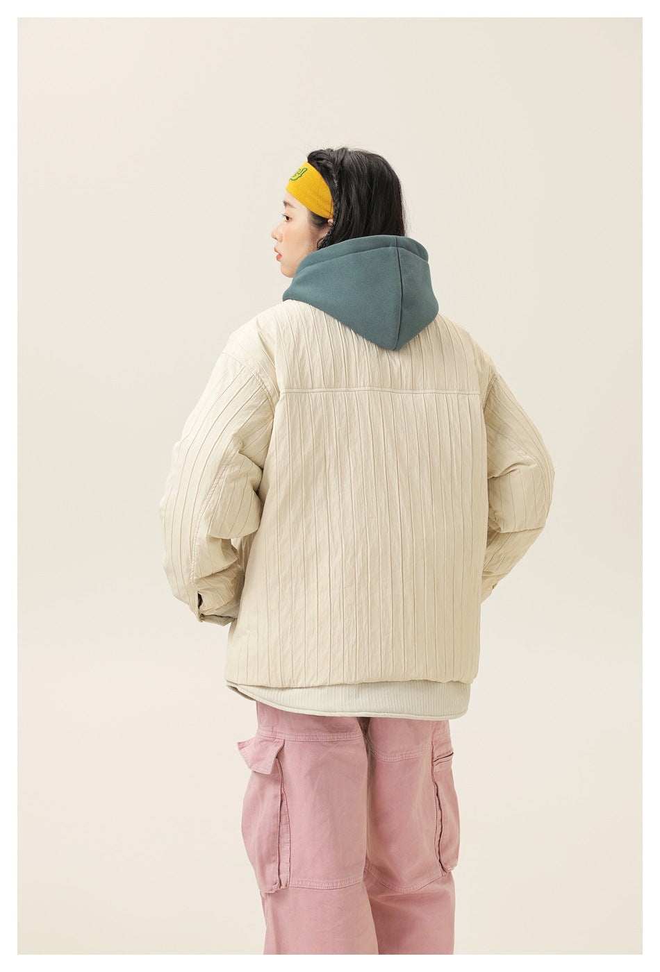 Back view of model wearing off-white quilted jacket over a teal hoodie with pink cargo pants