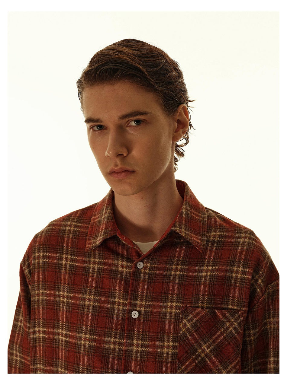 Close view of a model wearing a red-brown plaid shirt with a pointed collar and chest pocket.
