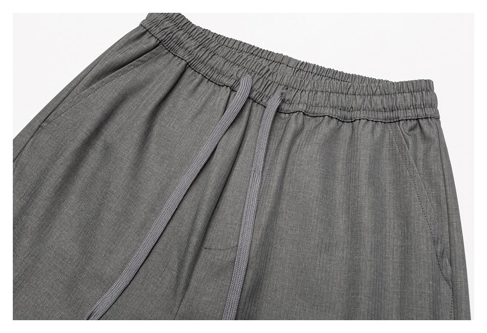 Close-up of gray pants showing the elastic waistband, drawstrings, and angled pocket opening.