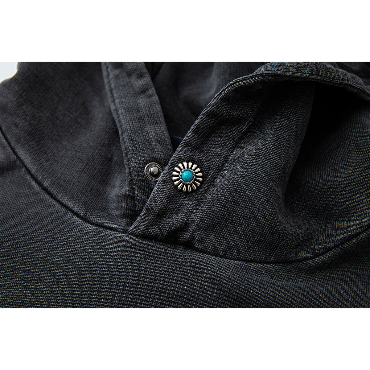 Close-up of a turquoise-and-silver decorative button and fabric at the charcoal hoodie's neckline.