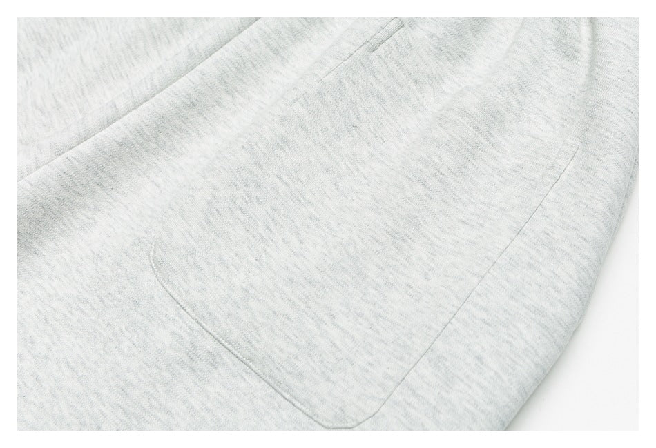 Close-up of light gray marl sweatpants with a large curved patch pocket and visible stitching.