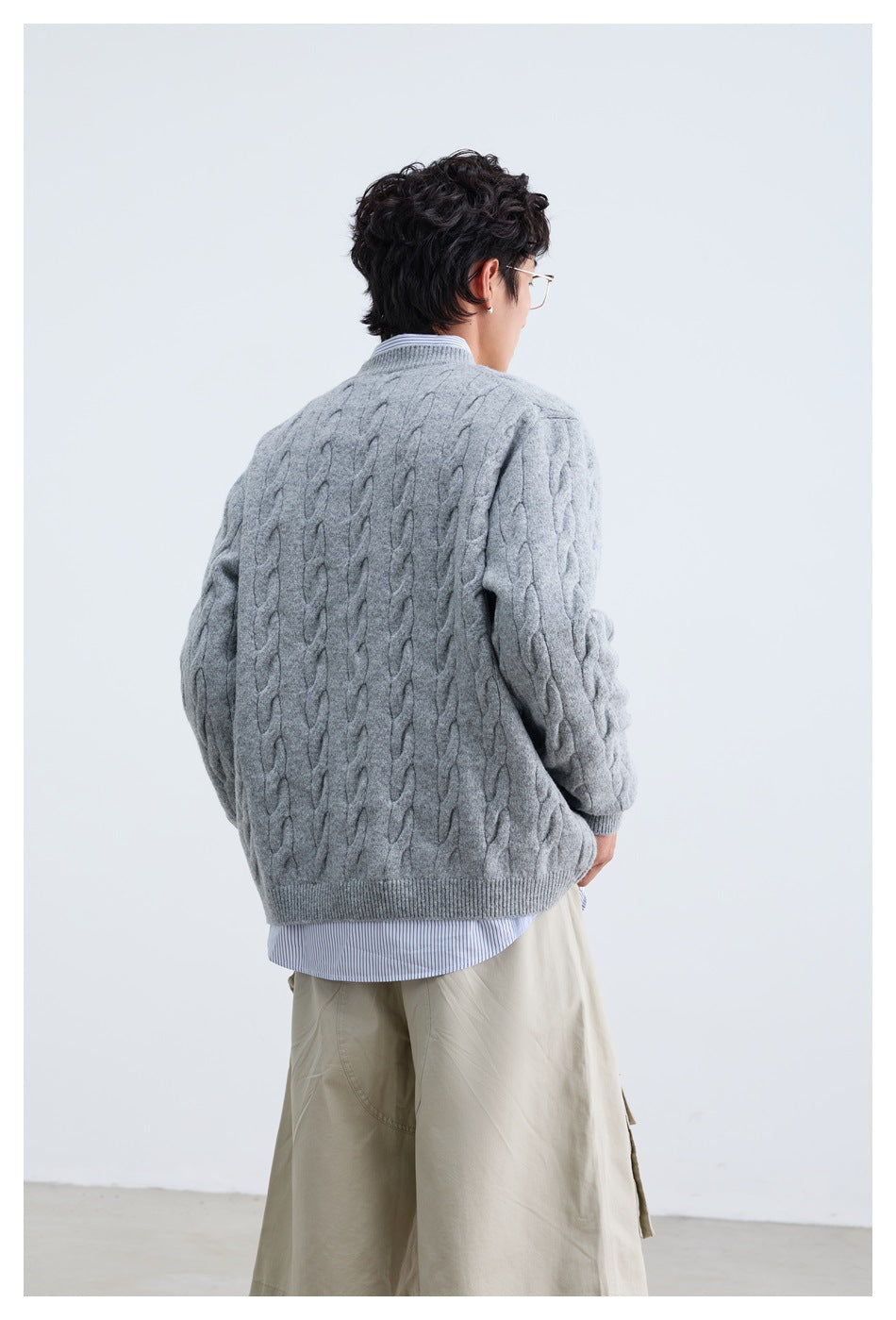 Back view of a person wearing a light gray cable-knit cardigan over a striped shirt.