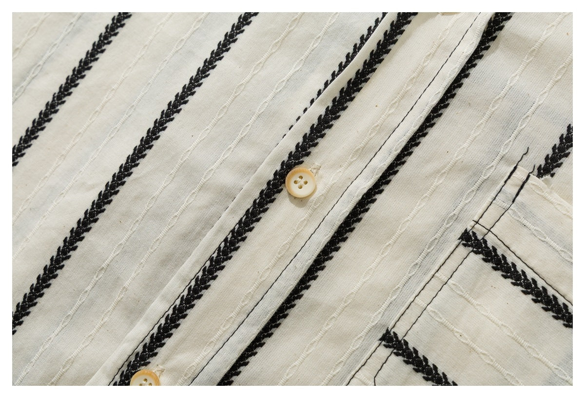 Close-up of ivory shirt fabric with black braided stripes, raised stitched lines, a button placket, and part of a pocket.