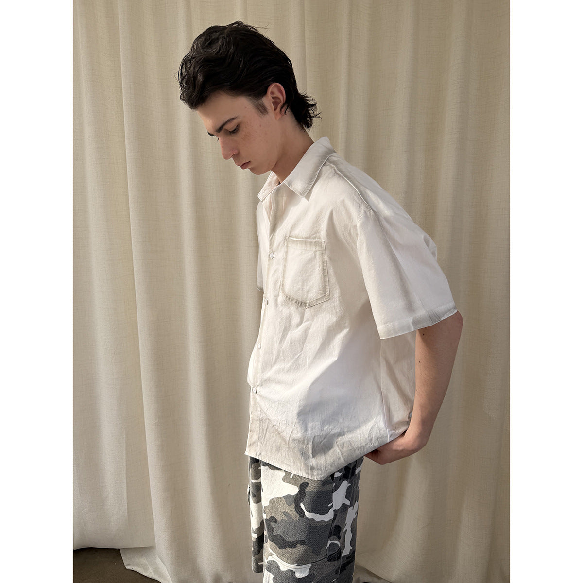 Side view of a model wearing a white short-sleeve button-up shirt and gray camouflage shorts.