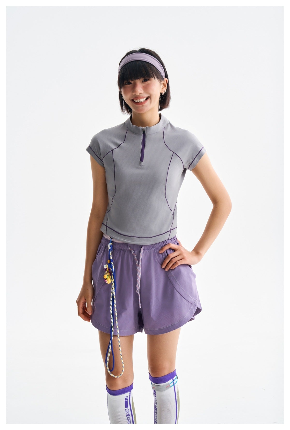Model wearing a gray zip-neck top with purple piping and lavender athletic shorts.
