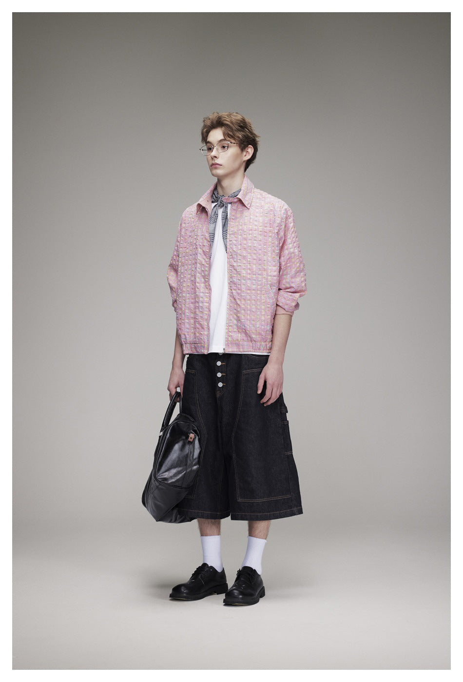 Model wearing the pink checked zip jacket open over a white tee with dark denim shorts, front view
