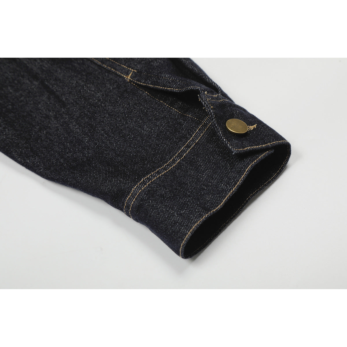 Close-up of a dark denim jacket sleeve cuff with contrast stitching and a gold-tone button.