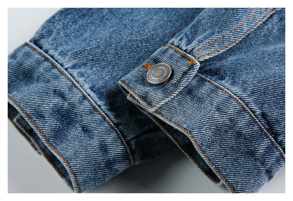 Close-up of a metal button fastening on a blue denim garment with orange stitching.