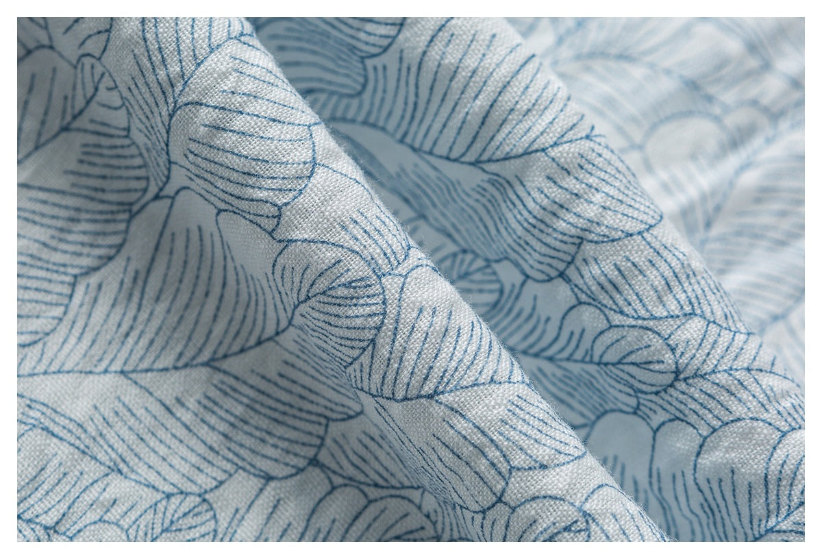 Macro view of folded pale blue-gray fabric showing its blue outlined leaf print and woven texture.