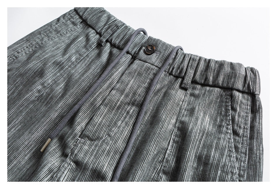 Close-up of gray textured pants showing the elastic waistband, button, belt loops, and drawstring.