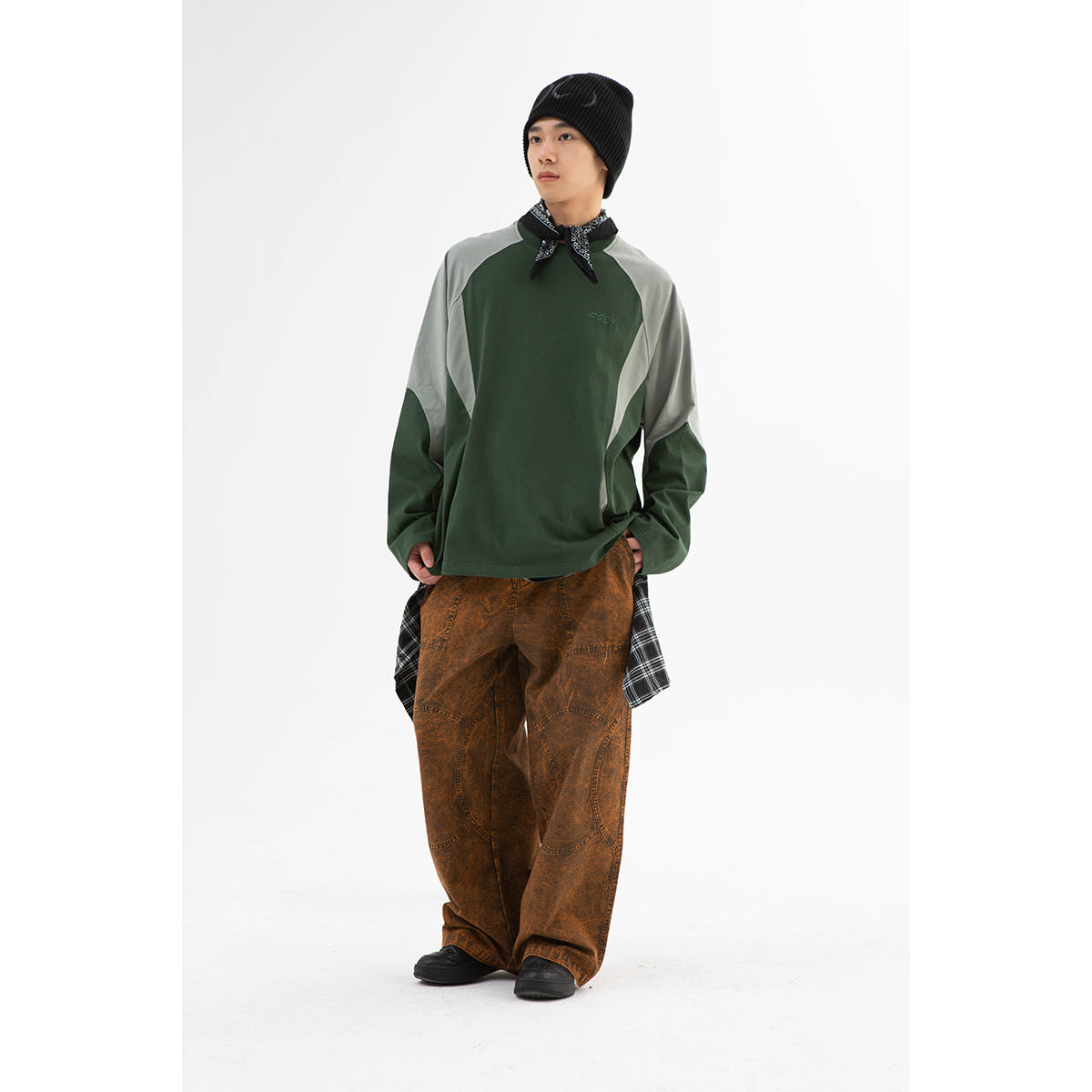 Model wearing a forest-green raglan sweatshirt with pale gray panels, styled with loose brown pants and a black beanie.