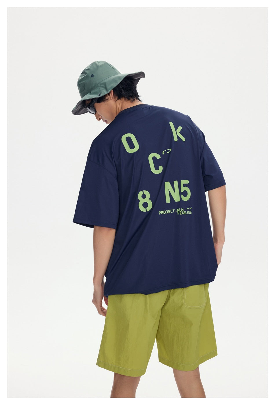 Back view of a model in a navy T-shirt with large lime lettering and graphics, paired with lime shorts.