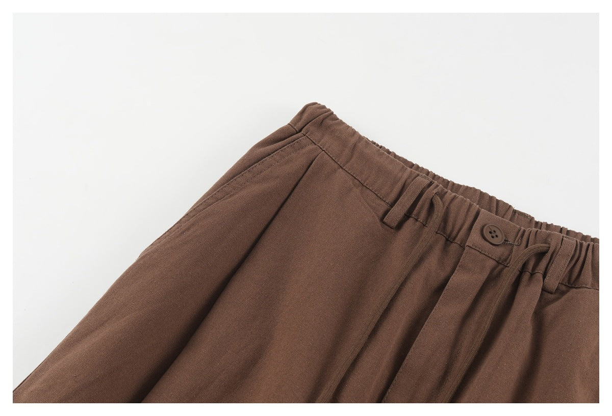 Close-up of the brown trousers' elastic waistband, button and front pleats.