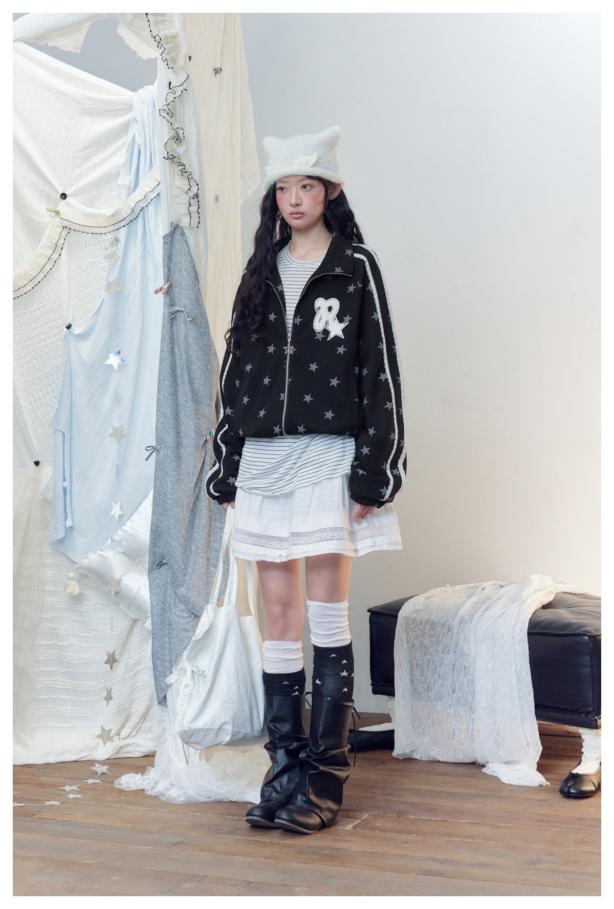 Model in the black star-print jacket with lace-trimmed sleeves, zipped, styled with a white skirt and fuzzy cat-ear hat