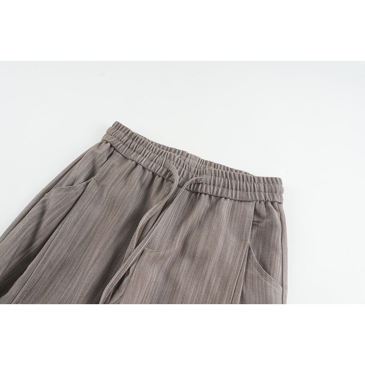 Close-up of taupe-gray trousers showing an elastic drawstring waist and angled side pockets.