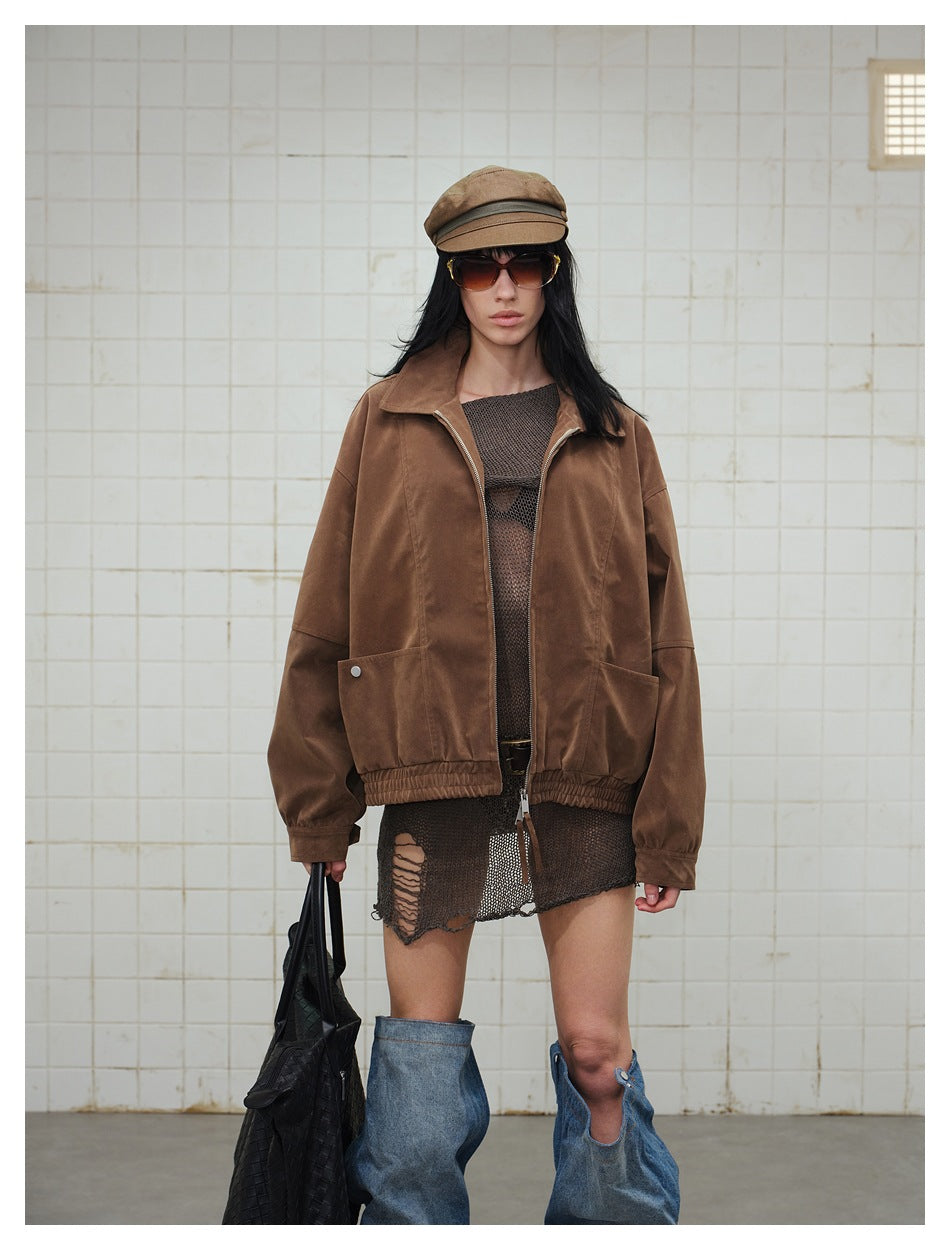 Model wearing an open brown zip jacket over a brown knit dress with a cap, sunglasses and black woven bag