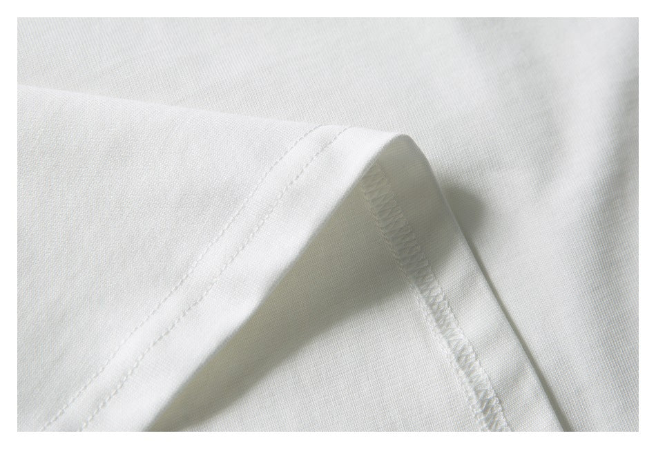 Macro view of a white T-shirt seam, showing the folded edge and overlock stitching.