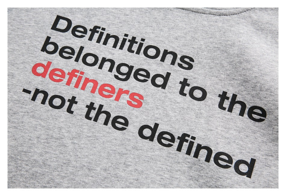 Close-up of a light gray sweatshirt print reading “Definitions belonged to the definers—not the defined,” in black and red.
