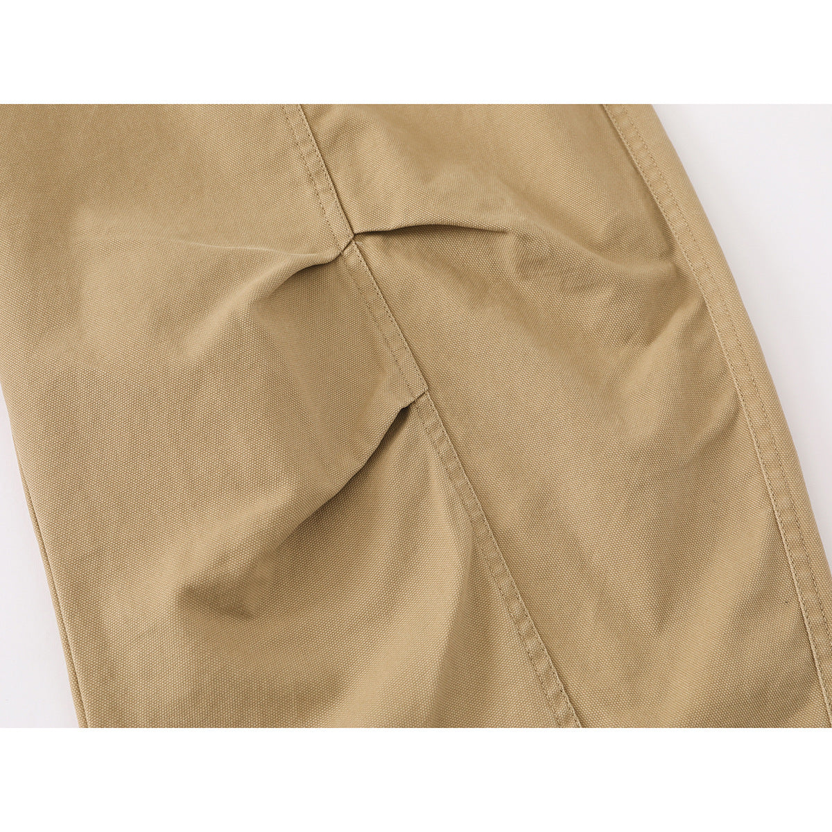 Close-up of tan trouser fabric with a stitched seam and angled panel detail.