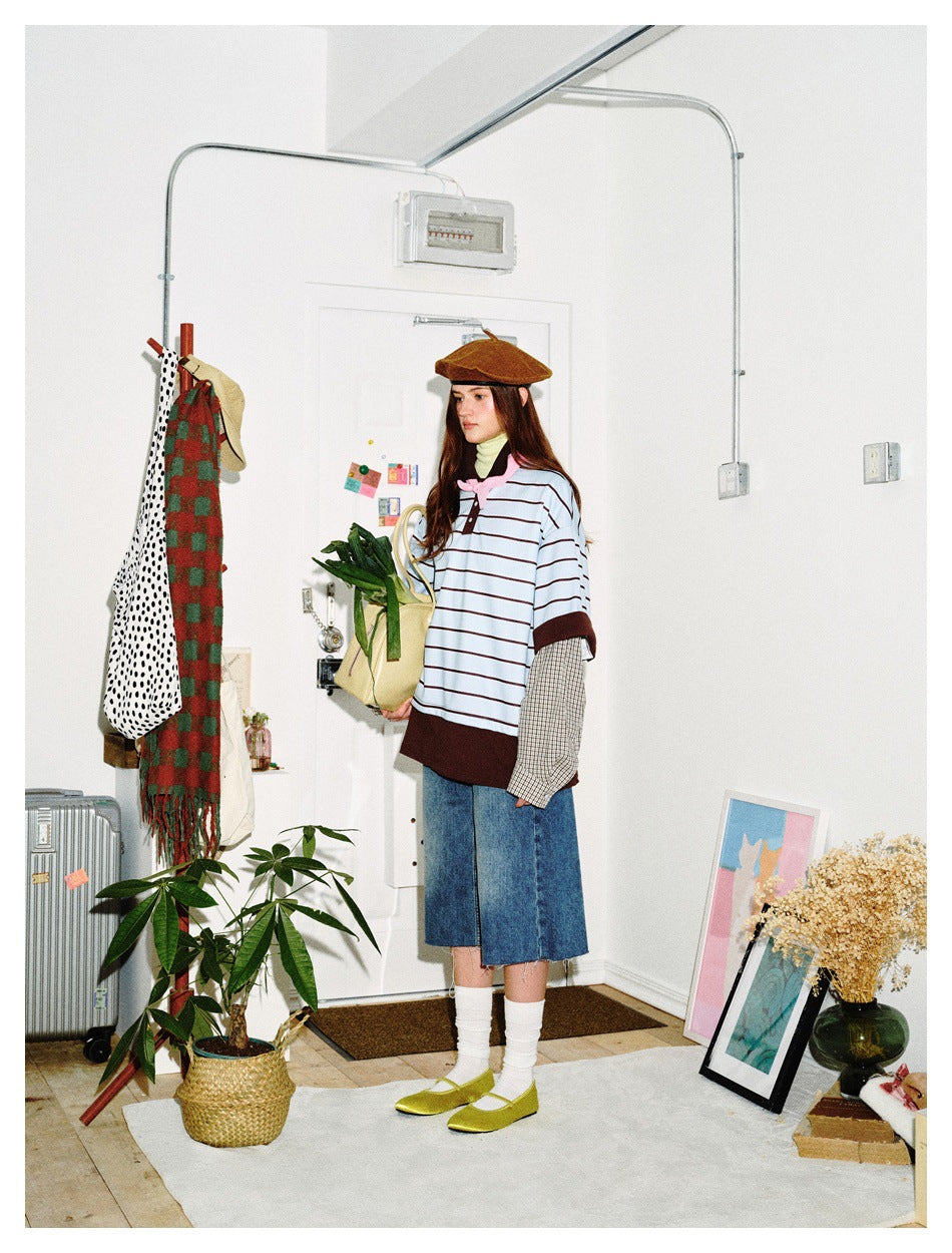 Side view of a model wearing an oversized light blue striped top with dark brown trim and layered checked sleeves.