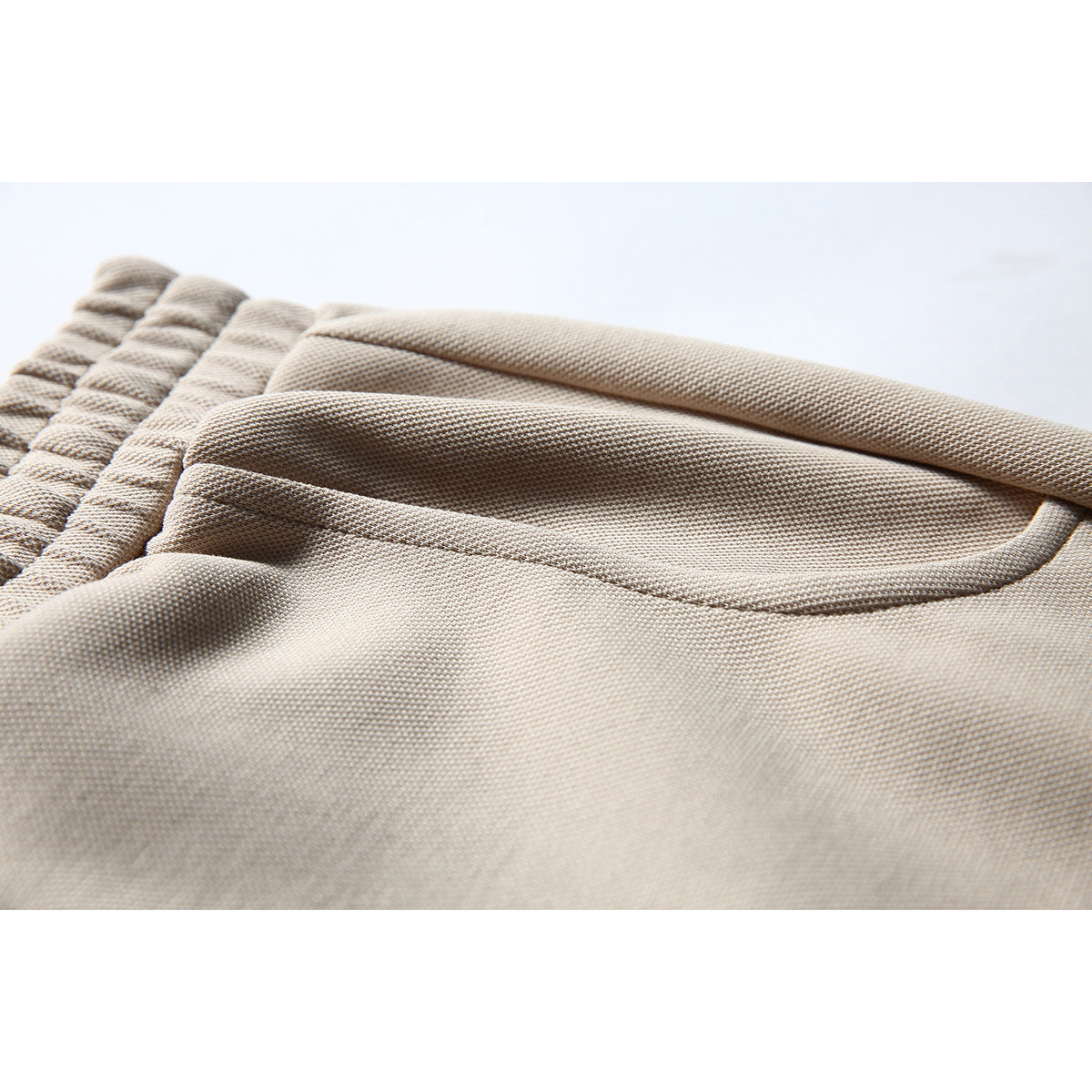 Close-up of the beige shorts' elastic waistband, fabric texture, and curved front pocket.