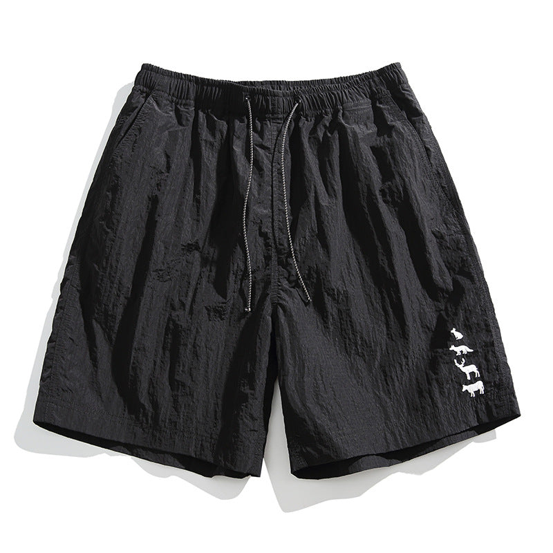 Black crinkled drawstring shorts with elastic waist and white animal embroidery on the lower leg, flat lay