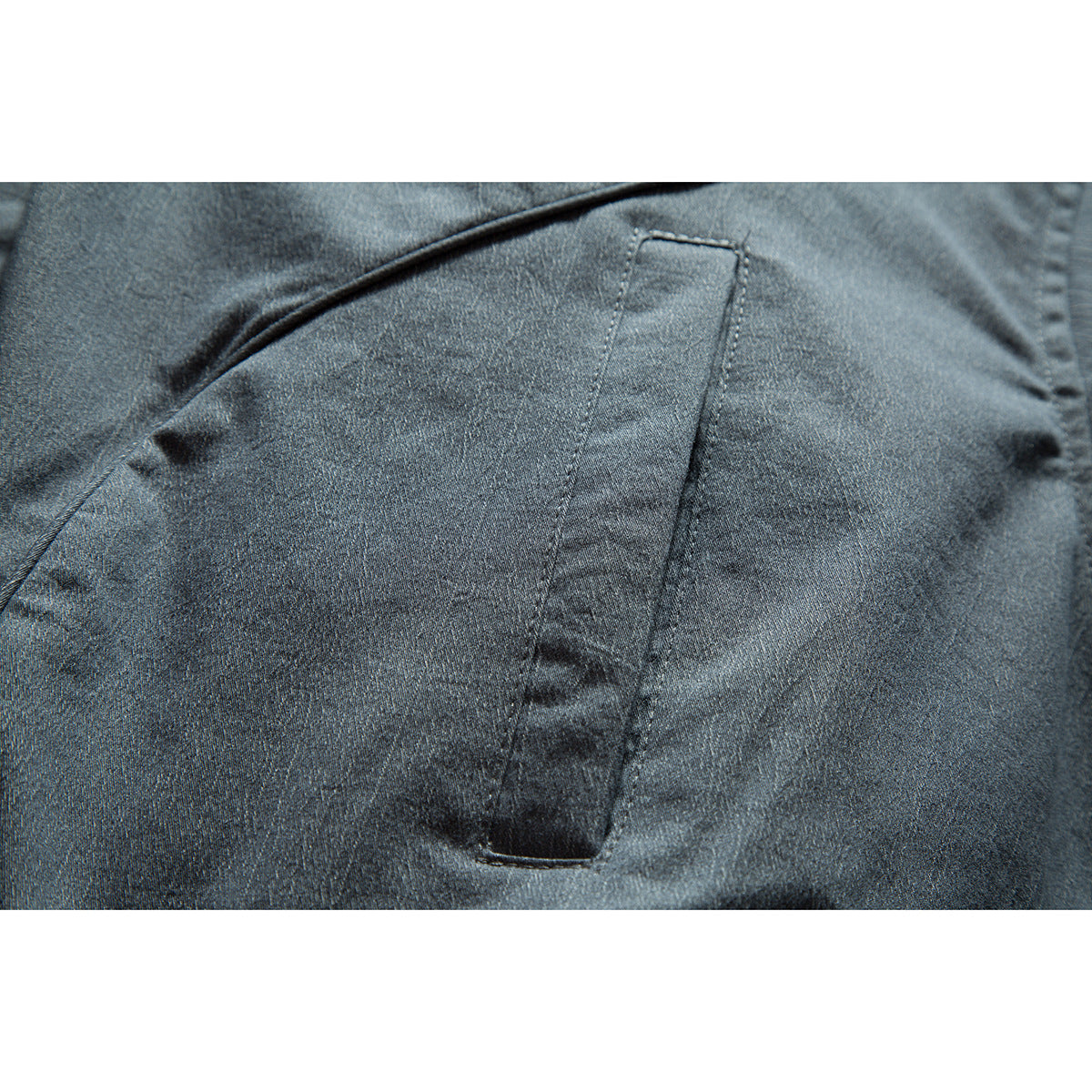 Close-up of a dark blue-gray jacket's angled seam and narrow vertical pocket.
