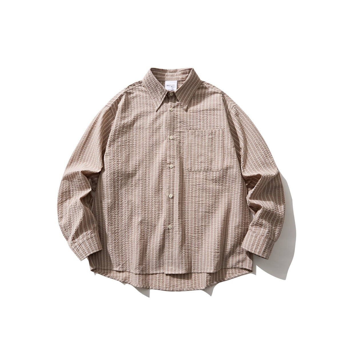 Light brown striped seersucker-style long-sleeve button-up shirt laid flat, with chest pocket and curved hem