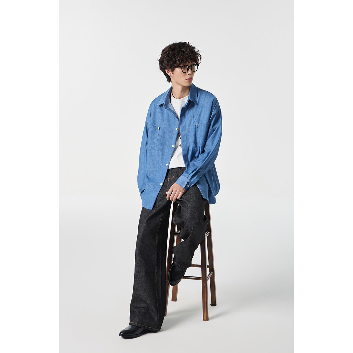 Full-length view of a model wearing a blue button-front shirt with chest pockets and dark wide-leg jeans.