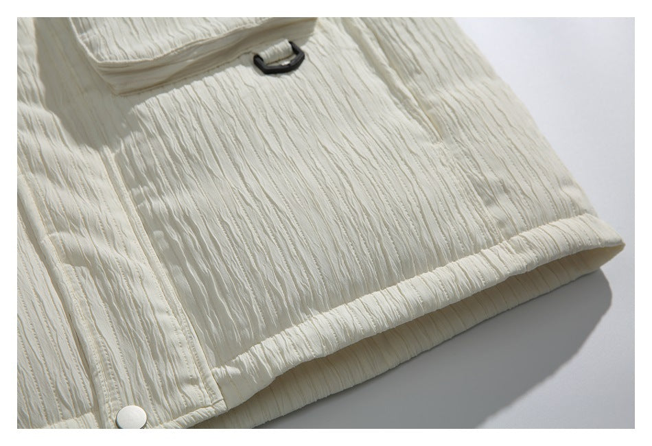 Close-up of an ivory textured jacket hem with a white snap and a small black tab.