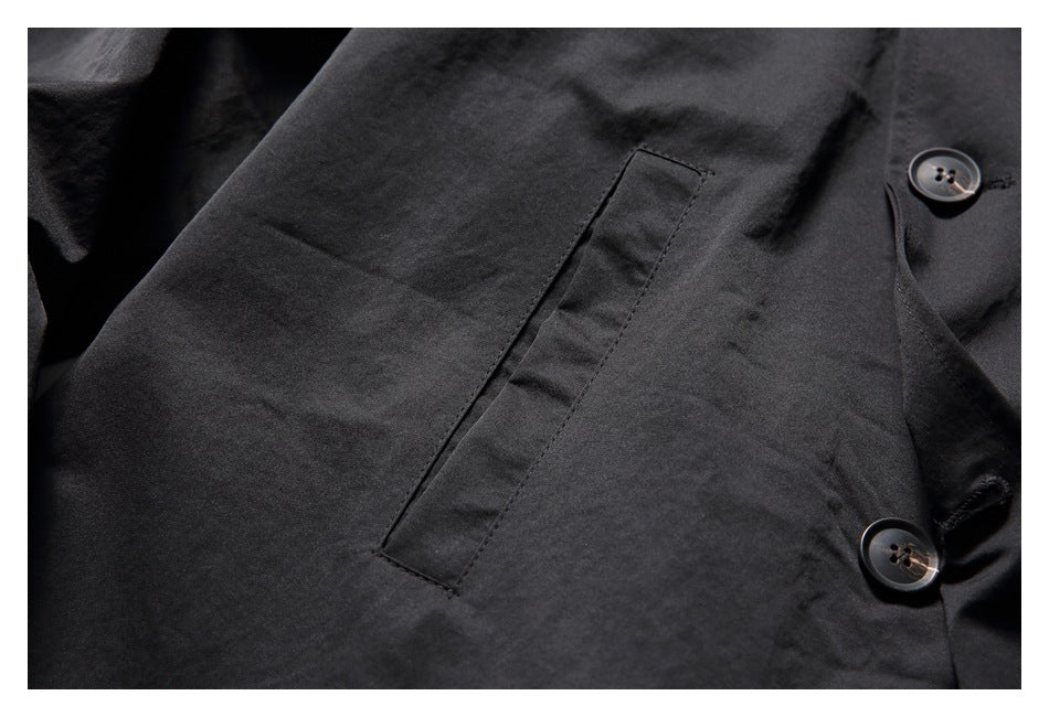Close-up of a slanted welt pocket and buttons on the black coat’s front.