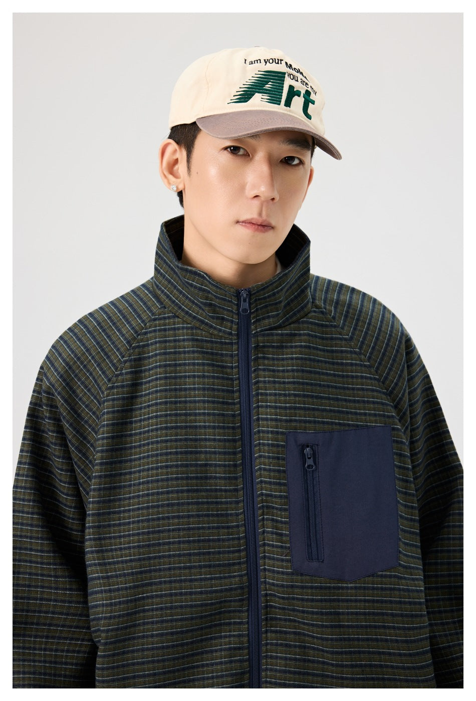 Close view of a model wearing a dark striped jacket with a stand collar and large navy zip chest pocket.