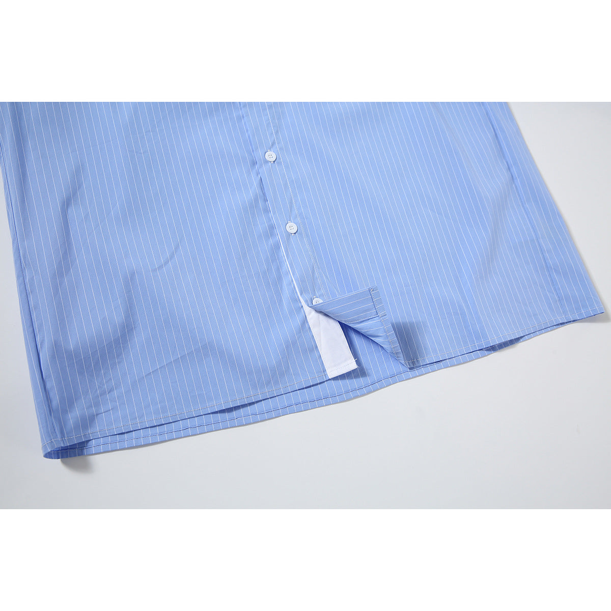 Close-up of the lower front hem of a light blue pinstriped shirt, showing buttons and a side opening.